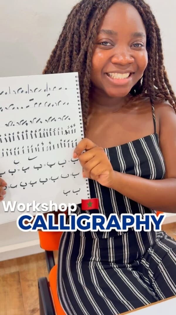 A student holding up her Arabic calligraphy practice sheet at an Al Minbar workshop