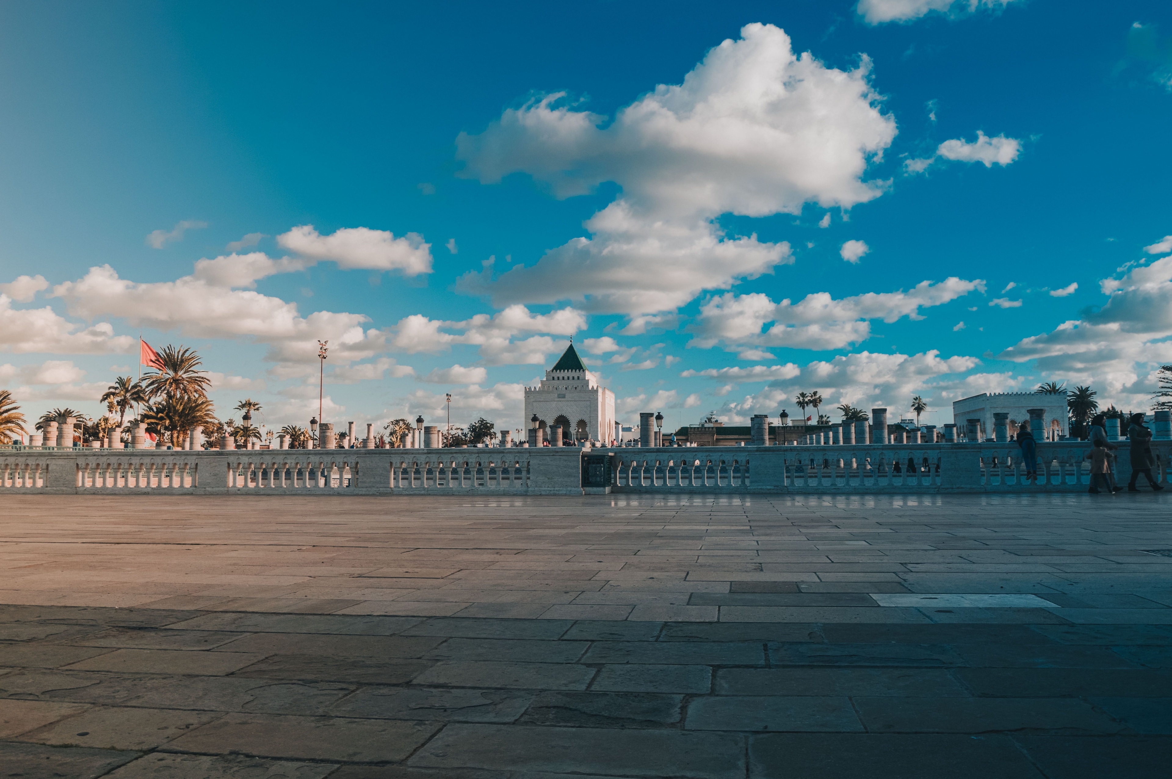 The Mausoleum of Mohammed V and its esplanade in Rabat, with palm trees and a Moroccan flag under a wide blue sky